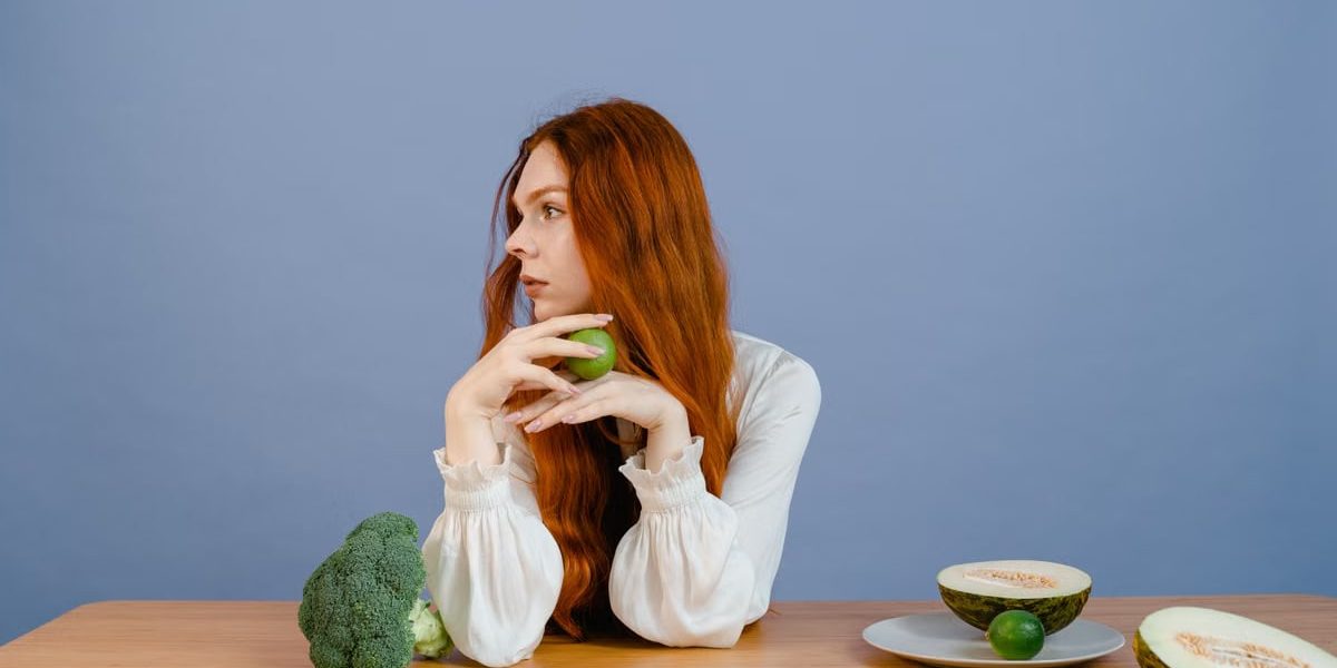 Thoughtful woman with broccoli, melon, and lime on a table.