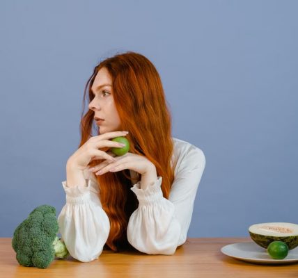 Thoughtful woman with broccoli, melon, and lime on a table.