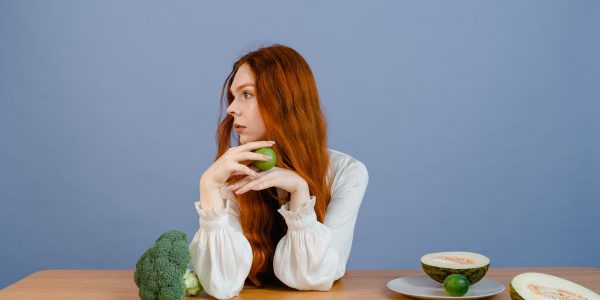 Thoughtful woman with broccoli, melon, and lime on a table.